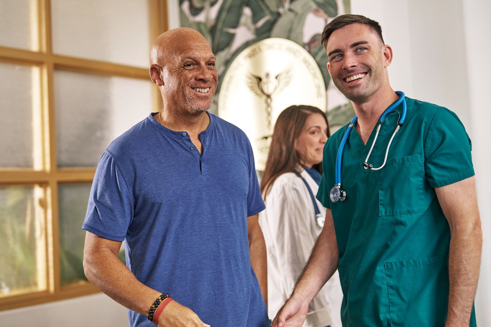 A smiling veteran talks with his doctor and a nurse in a CareSource Military & Veterans network clinic