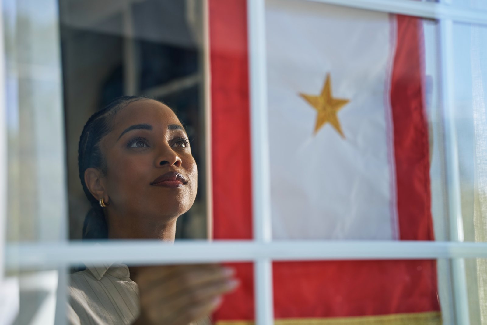 A woman looks out a window beside a Gold Star service flag