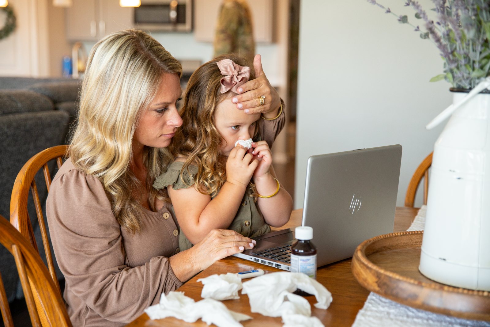 A military spouse checks her sick daughter’s temperature during a telehealth visit at the kitchen table