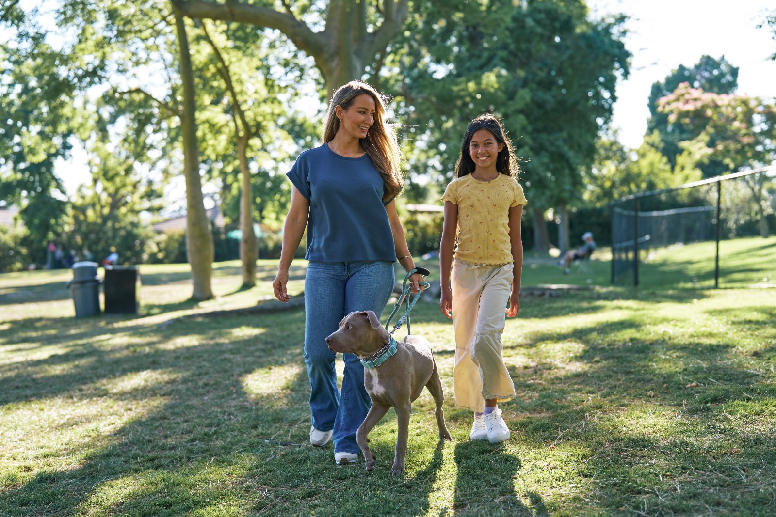 A mother and daughter walk their dog through a sunny park
