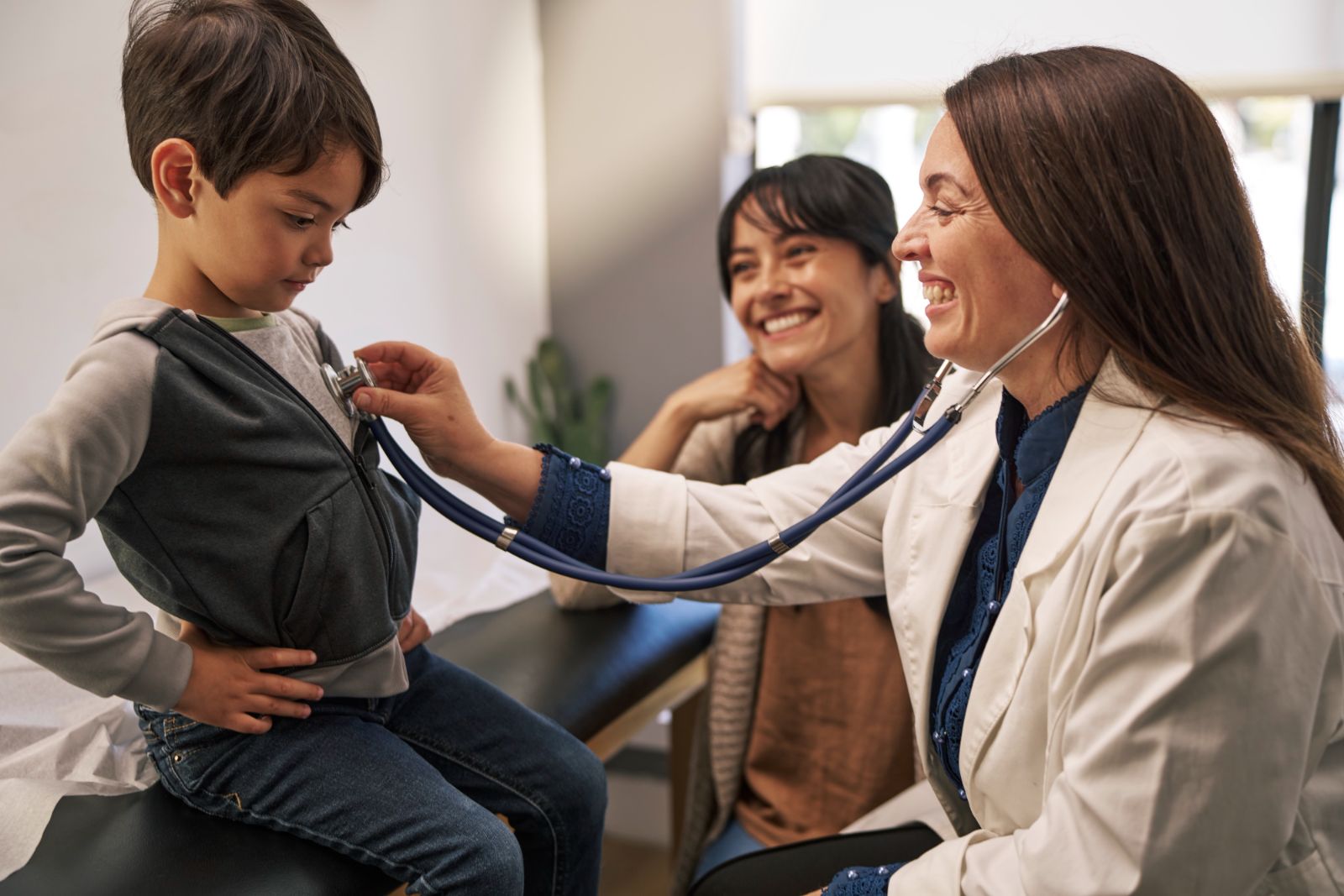 A pediatrician listens to a young boy’s heartbeat while his mother smiles during a TRICARE Prime Demo network visit