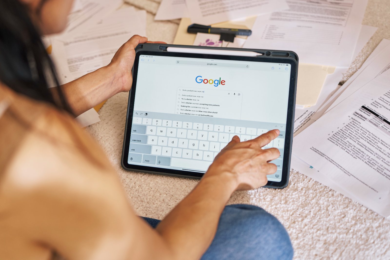 A woman searches for a doctor on her tablet surrounded by health plan paperwork